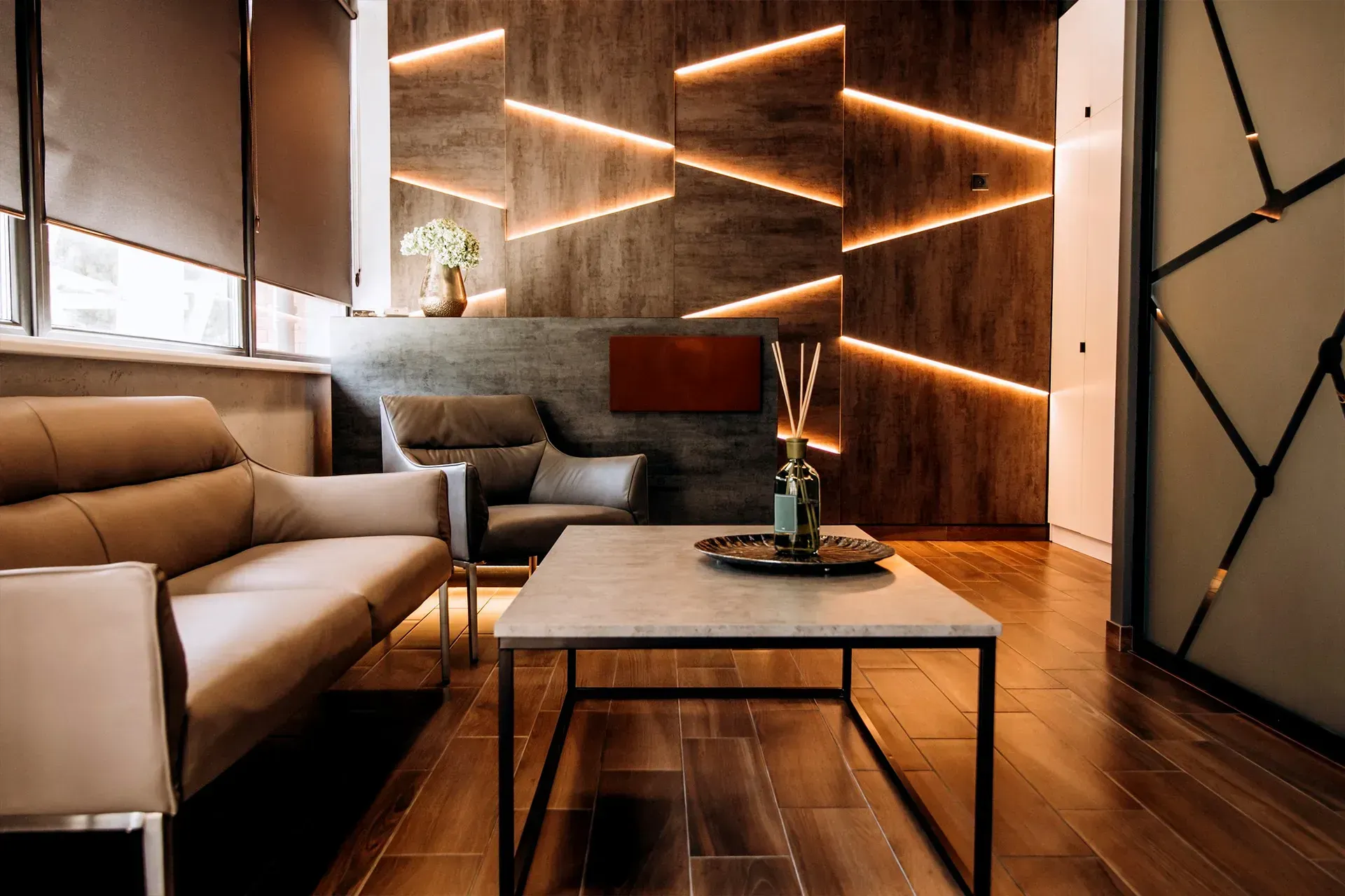 Modern lounge with beige sofas, glass coffee table, wood floors, and geometric LED wall lighting.