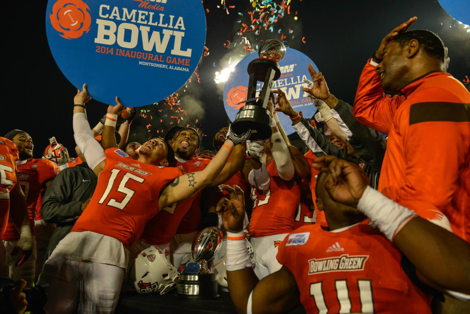 A group of football players holding a trophy in front of a sign that says camellia bowl