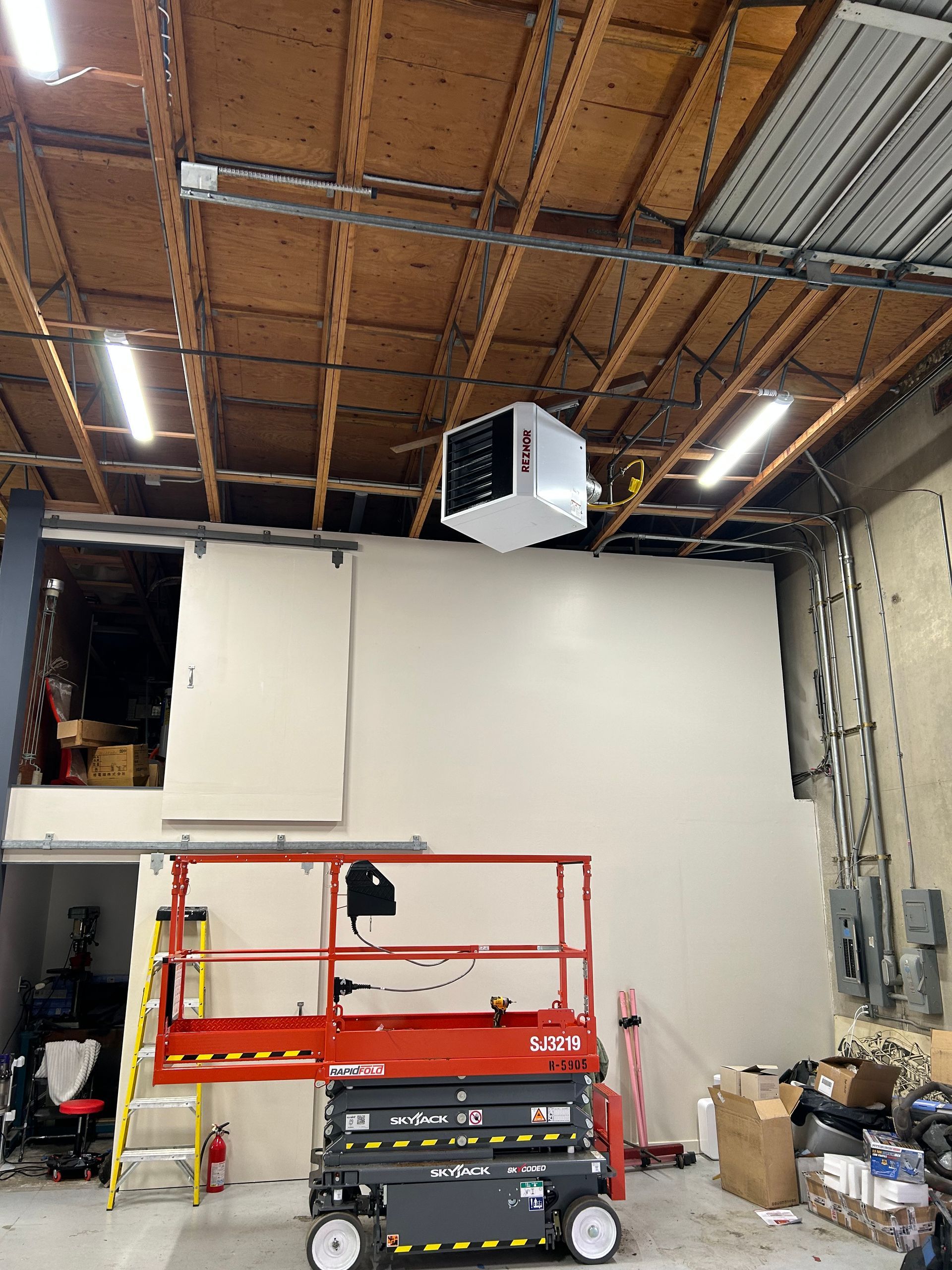 Warehouse interior with white wall panels, red lift platform, and tools under exposed wooden ceiling