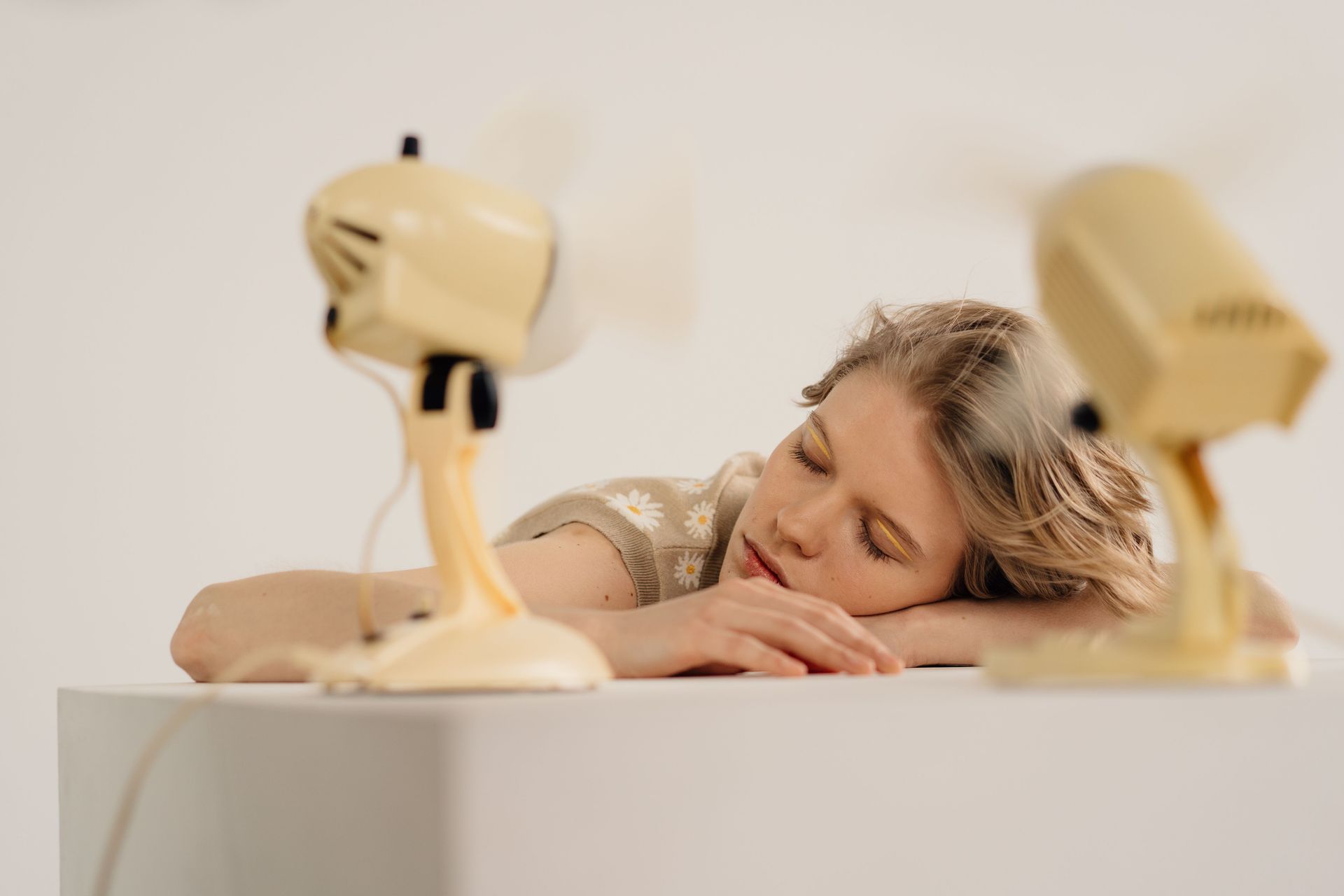Sleepy person resting on a counter between two fans in a warm indoor room
