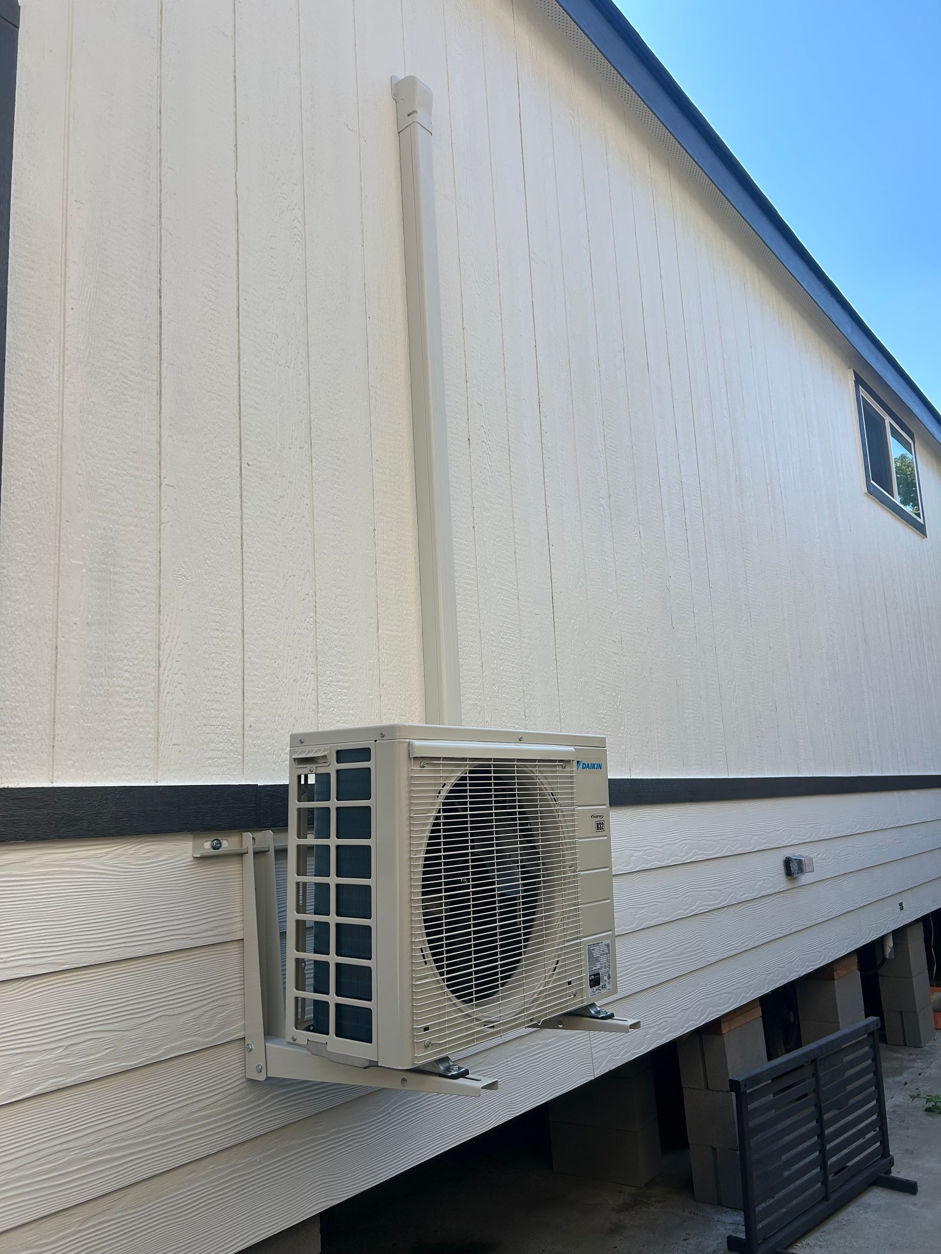 Wall-mounted air conditioner unit on the side of a beige mobile home under a blue sky