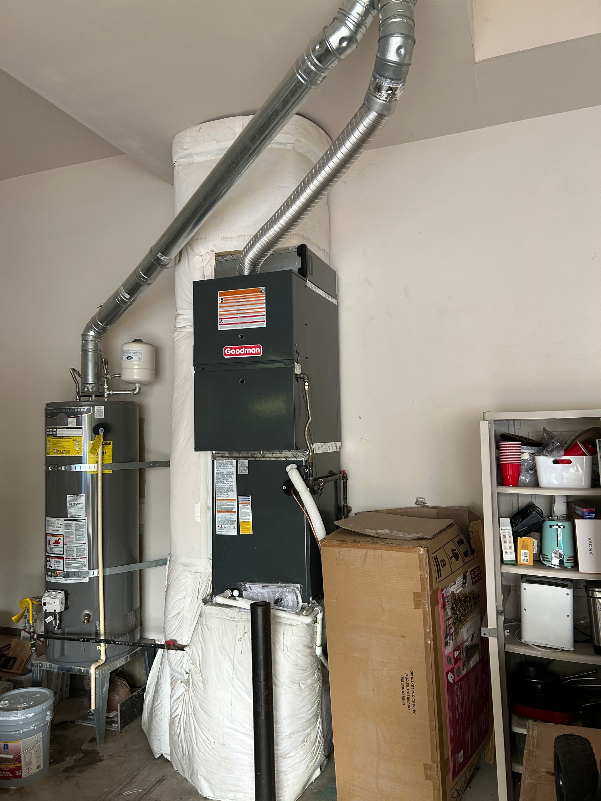 Basement furnace and HVAC ducts beside shelving and stored boxes in a utility room