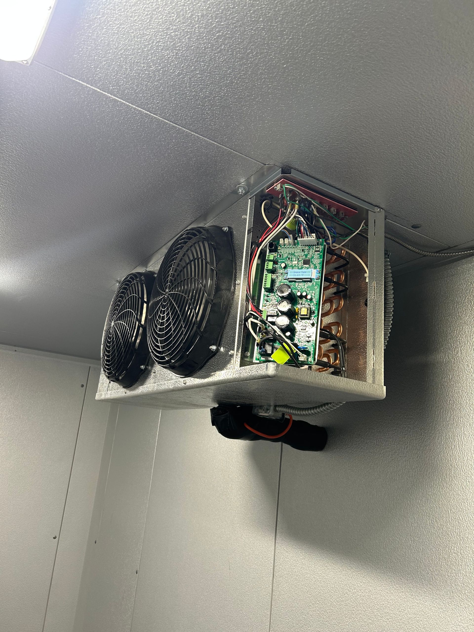 Electronics mounted near a ceiling, with exposed wires and two black cooling fans in a metal enclosure