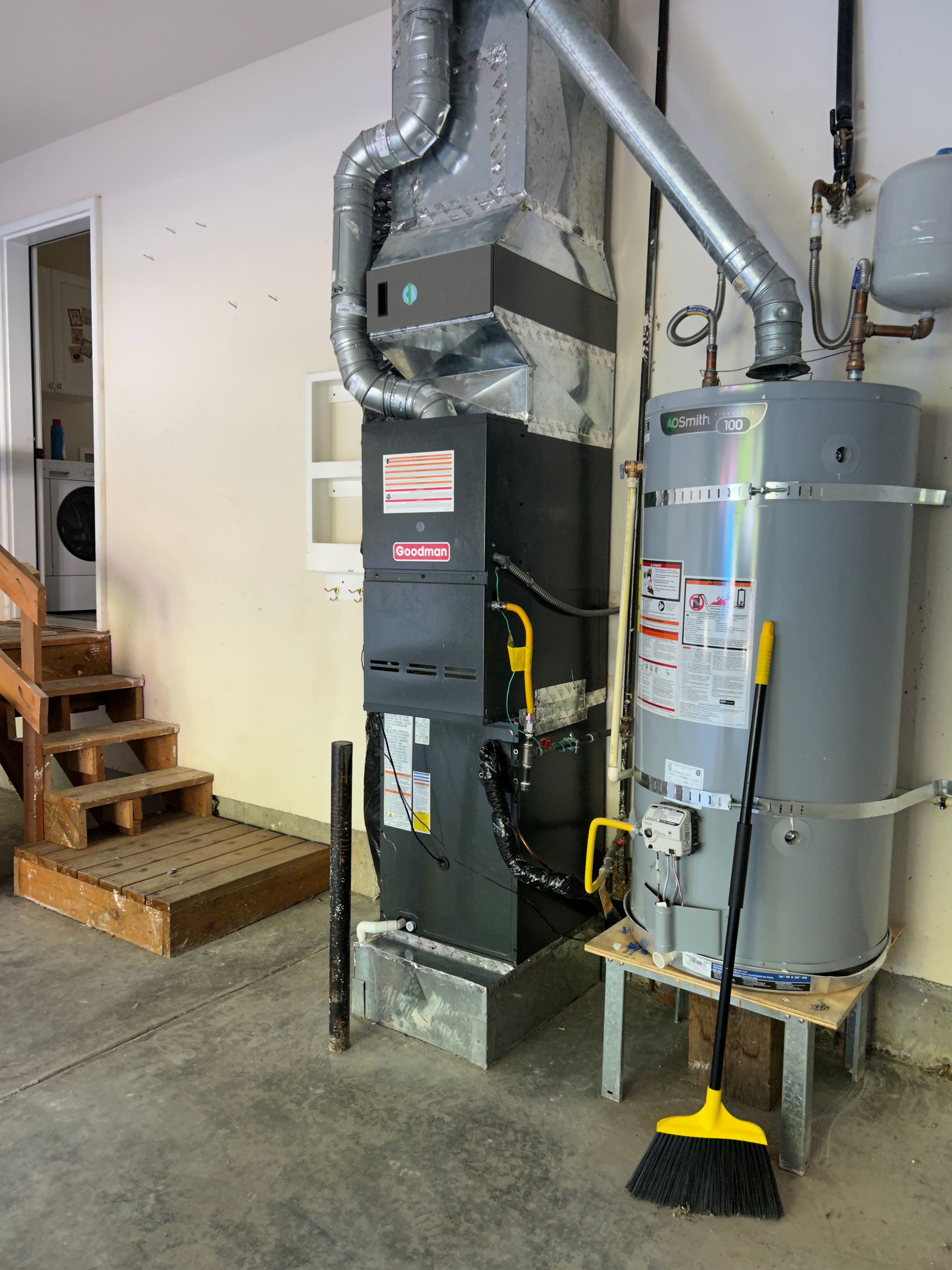 Basement utility room with furnace, water heater, and exposed ducts beside stairs.