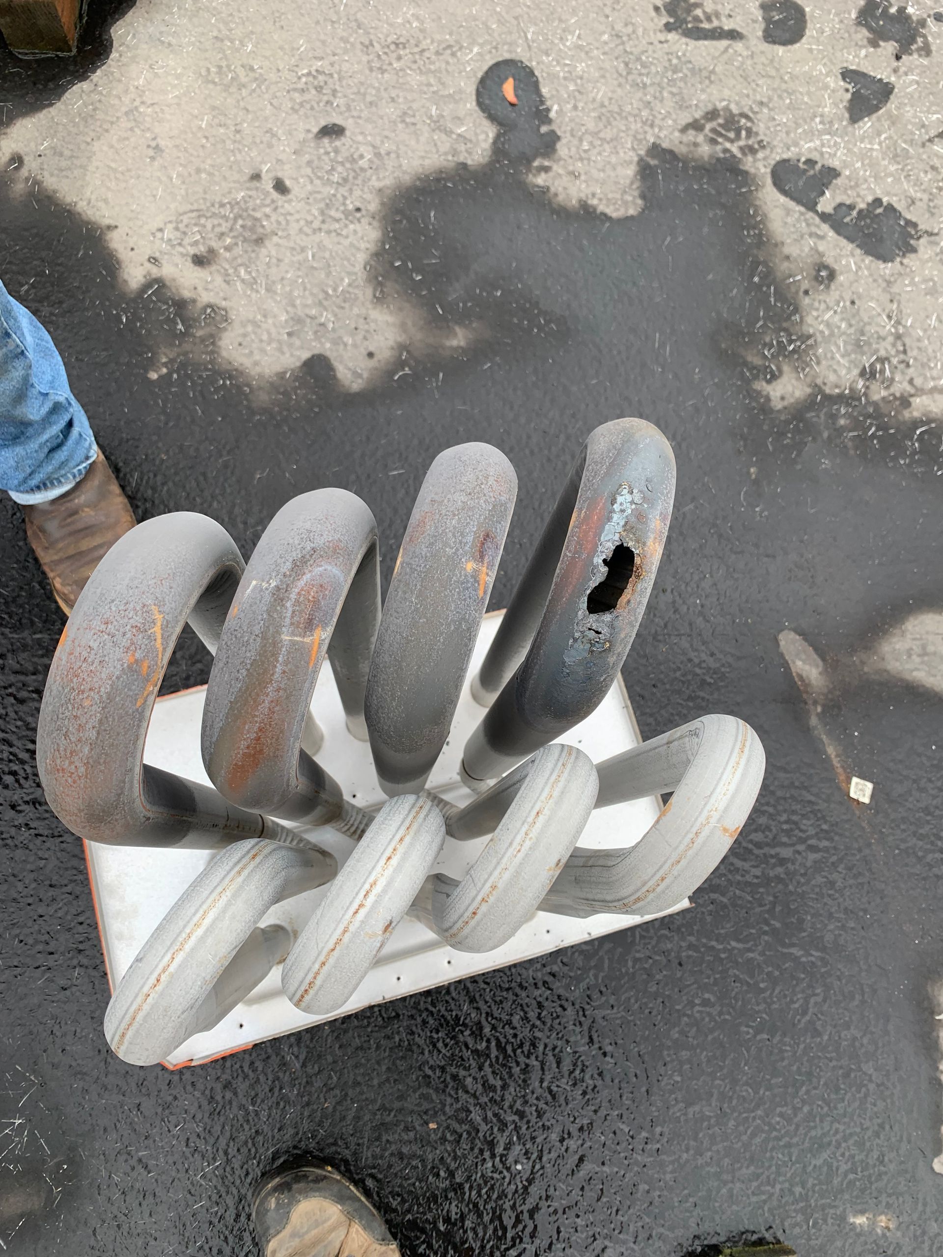 Gray and white coiled metal spring on wet pavement, with a person's shoe at left.