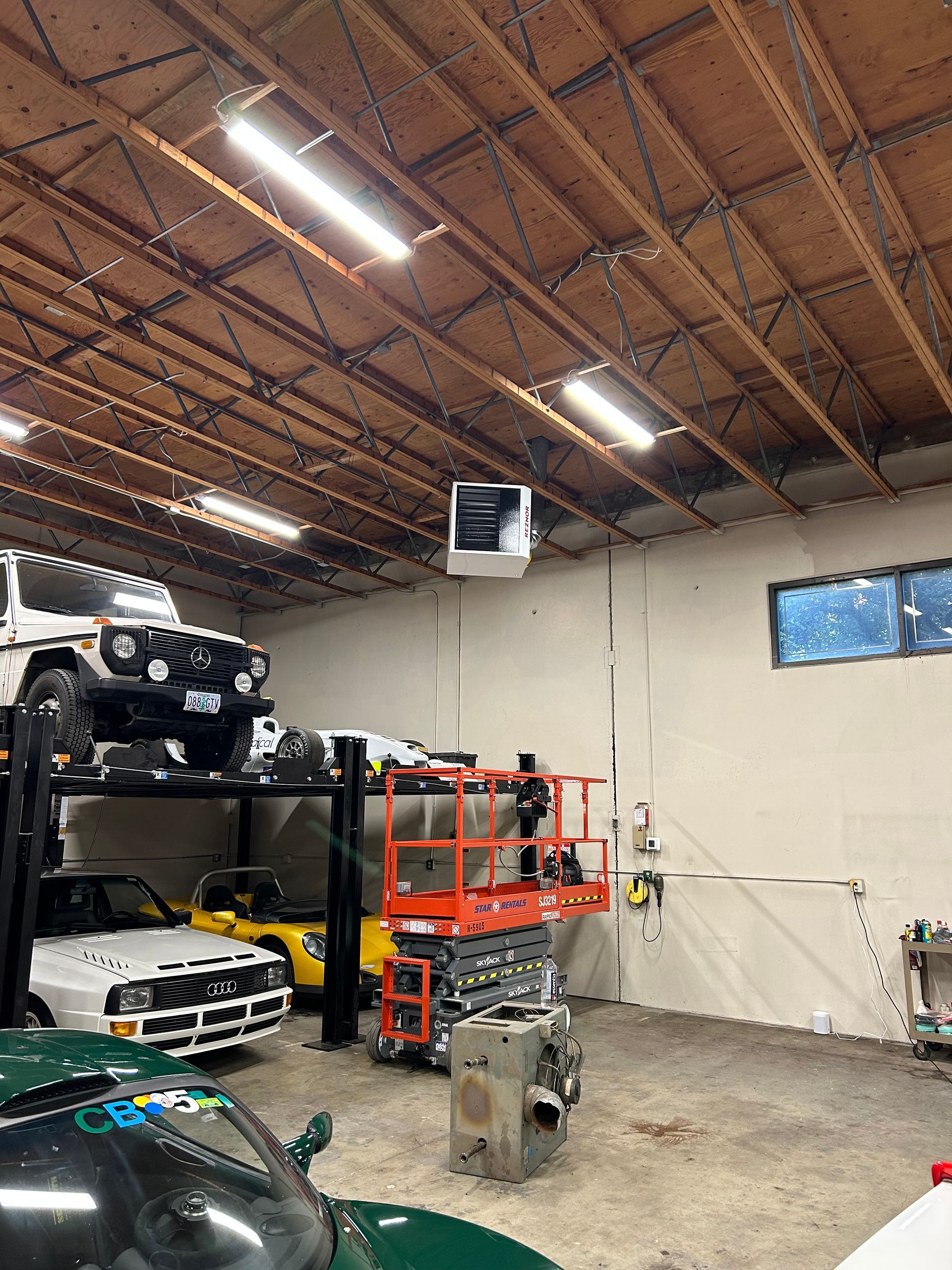 Auto repair garage with car lifts, shelves, tools, and a red lift near a white wall and ceiling lights