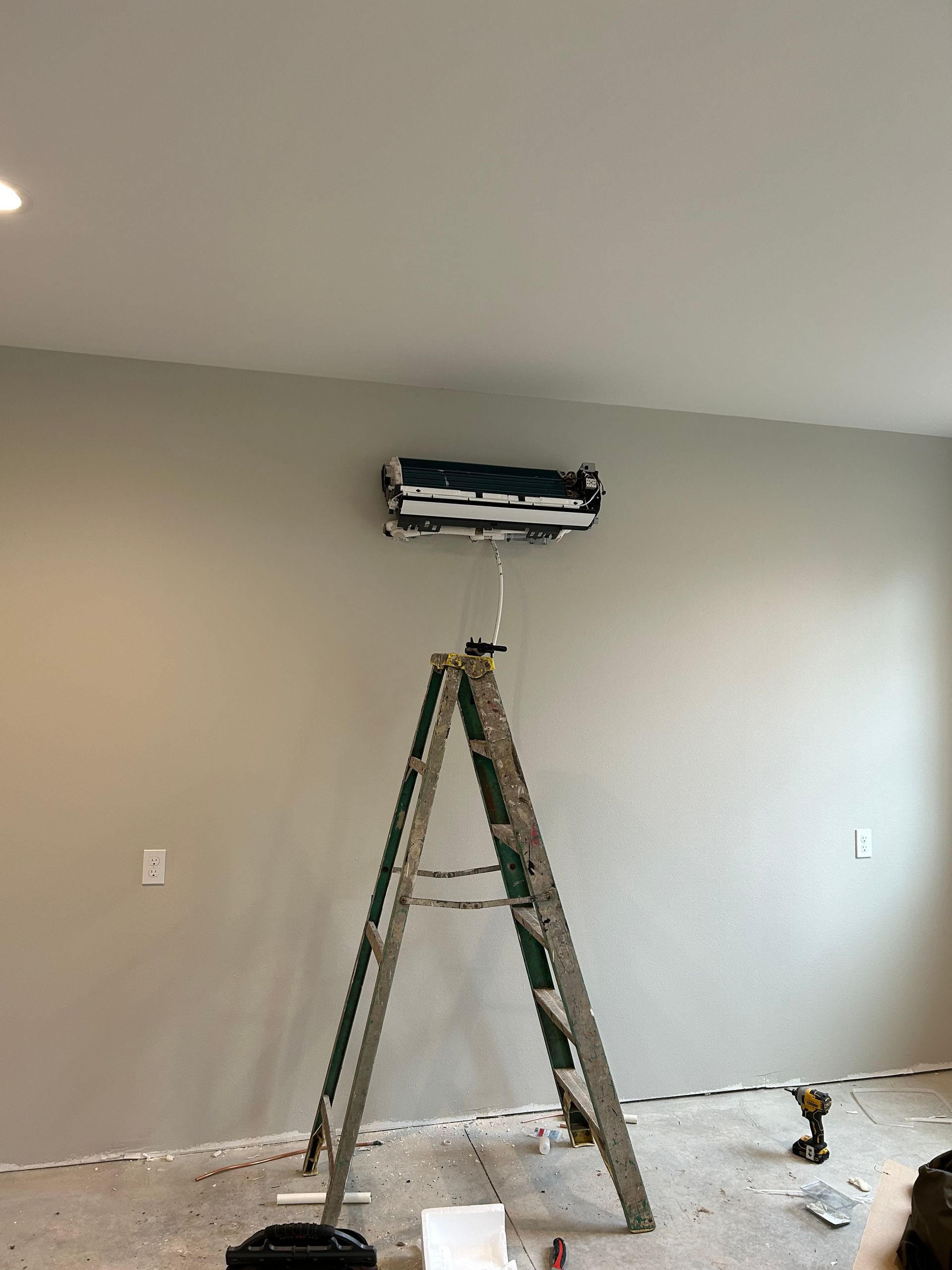 Worker painting a beige wall with a ladder in a room under renovation