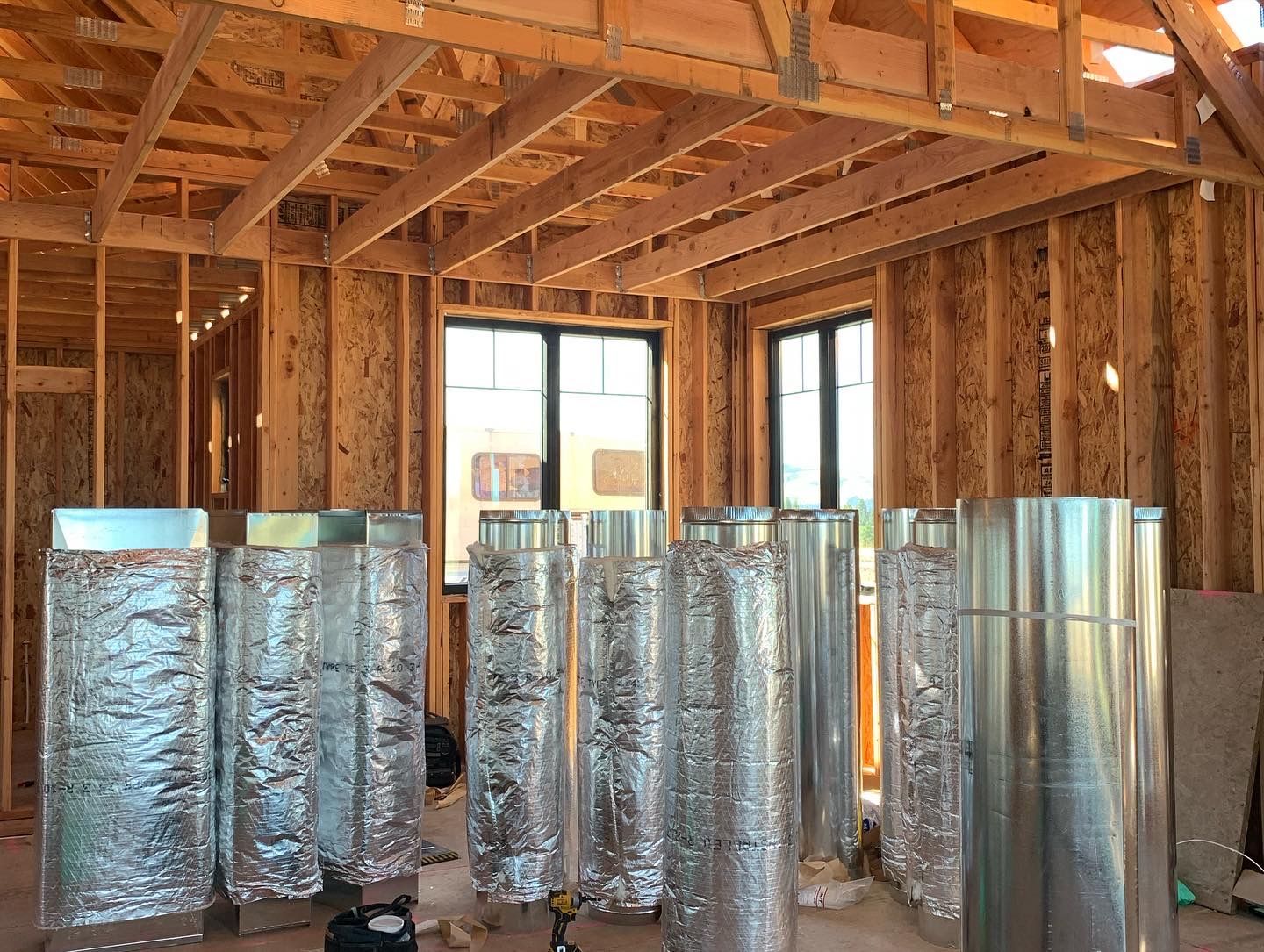 Unfinished home interior with exposed framing and HVAC ducts, viewed through a partially built room.
