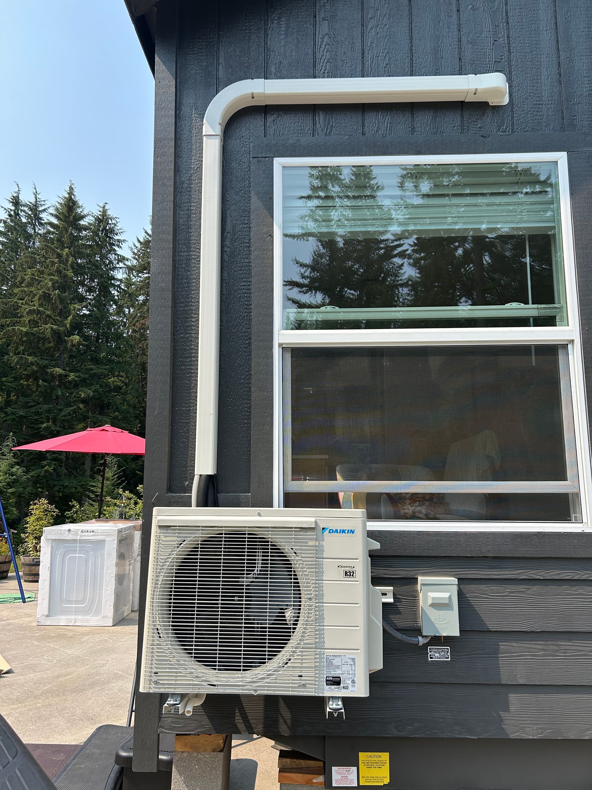 Outdoor building wall with window and air-conditioning unit, with a pink patio umbrella in the background.