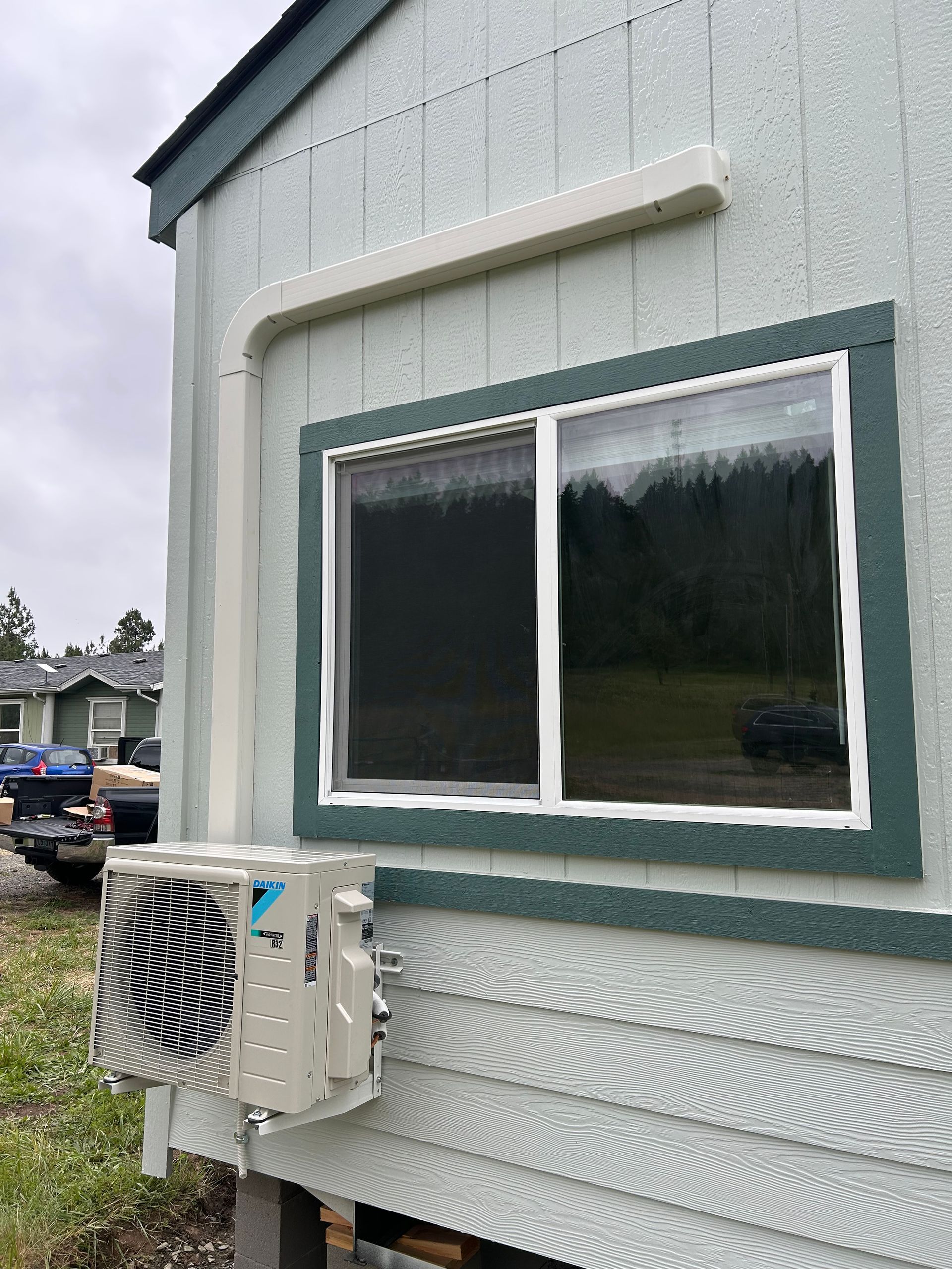 Exterior of a light gray house with a window and a mounted air conditioner unit under cloudy skies