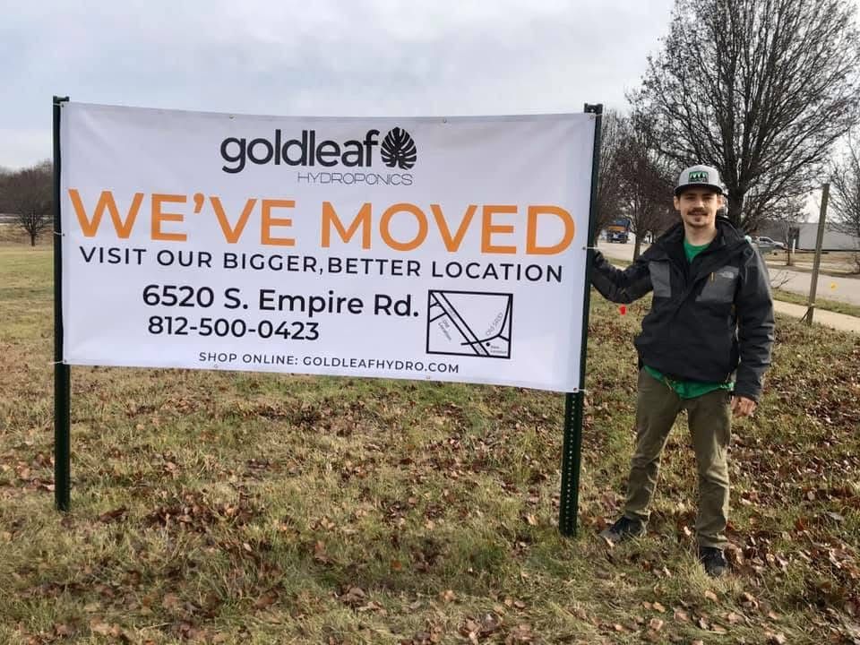 Goldleaf employee beside “We’ve Moved” sign at roadside, with new address and phone number.