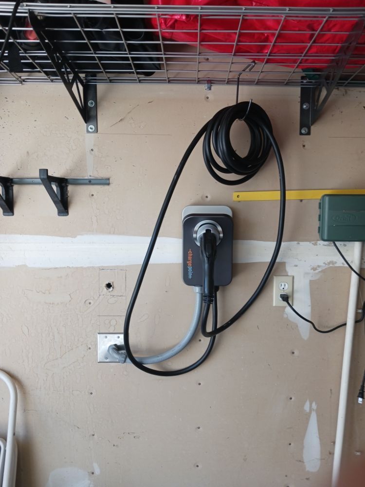Electric vehicle charger mounted on a garage wall, with coiled black cable and gray charger unit.