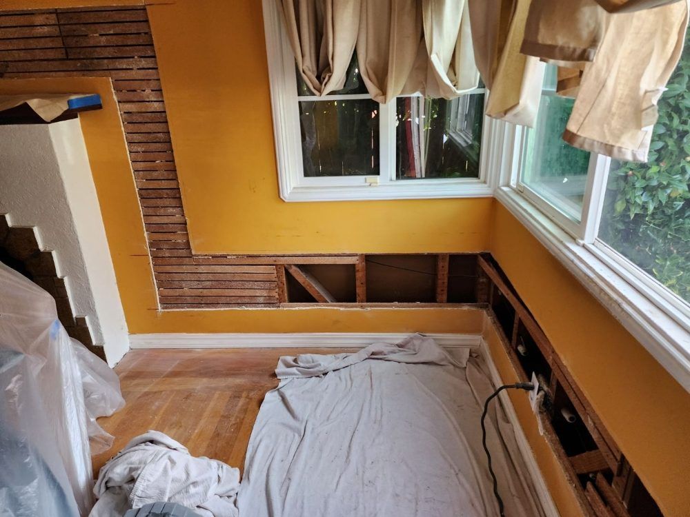 Room under renovation with exposed wall studs, yellow walls, and a window.