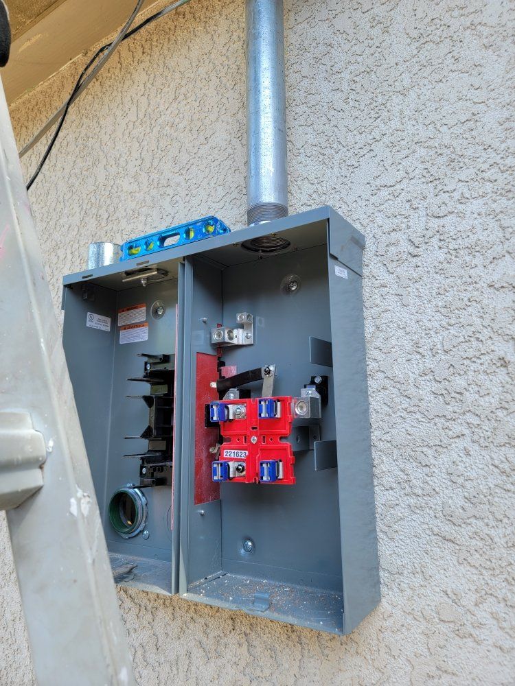 Gray electrical panel mounted on a beige stucco wall with conduit and red circuit breakers.