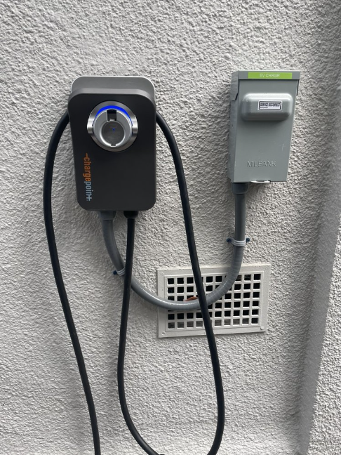 Wall-mounted NeoCharge EV charger and electrical box on a white wall. Black charging cable.