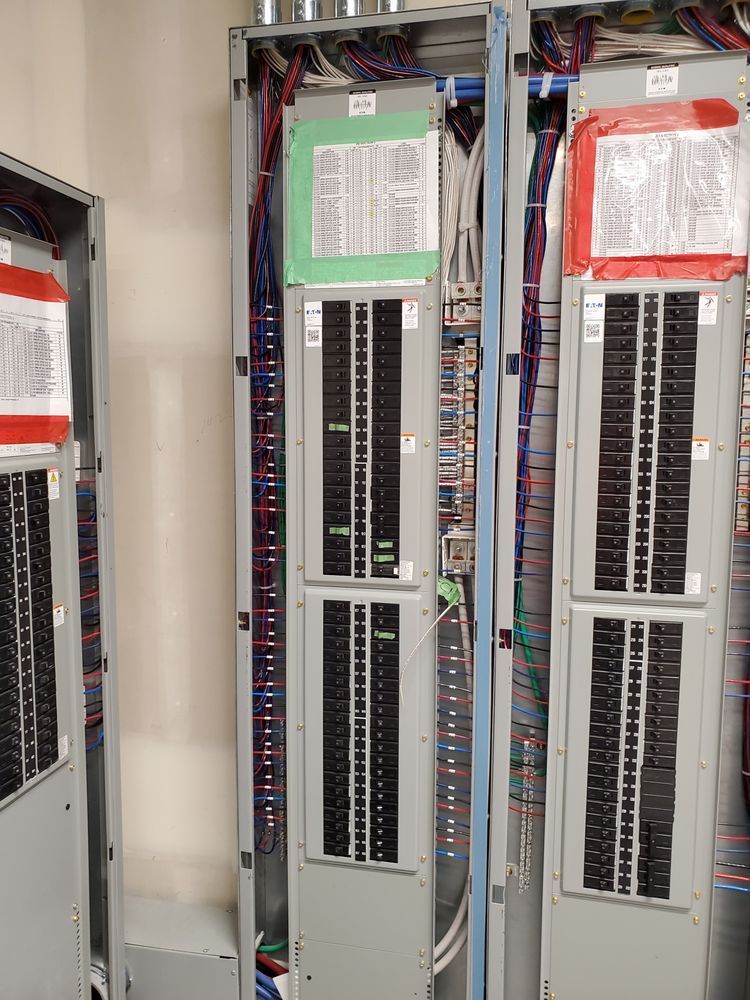 Electrical panels with numerous circuit breakers, wires, and labels. Gray metal cabinets in an indoor setting.