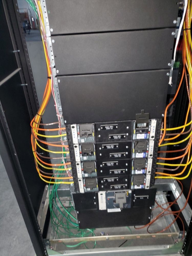 Server rack with black boxes, orange and green cables.