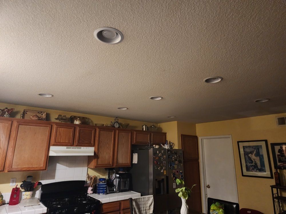 Kitchen interior: Recessed ceiling lights, wood cabinets, black stove, refrigerator, yellow walls.