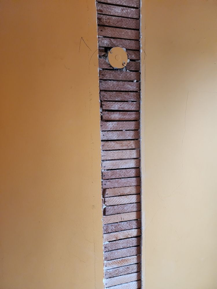 Yellow painted walls flanking exposed brick and lathe with a circular hole.