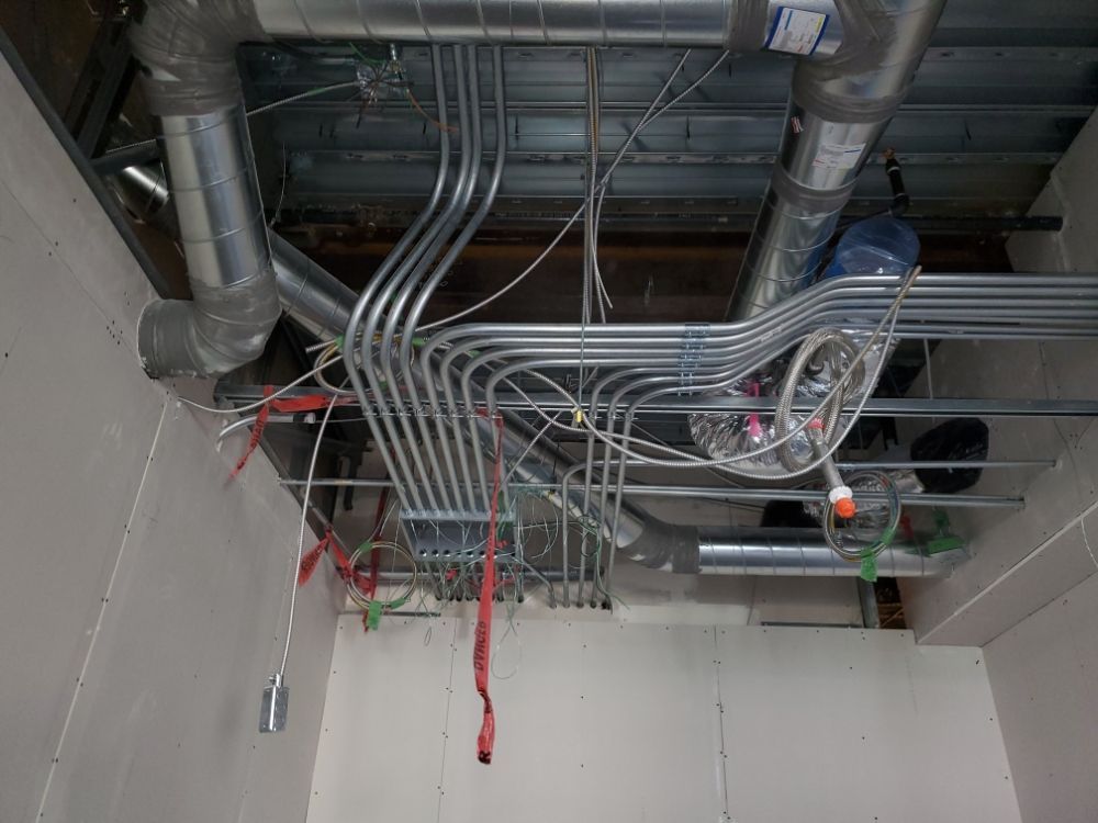 Ceiling view: metal conduits and ductwork installed. Electrical wiring and other utilities visible.