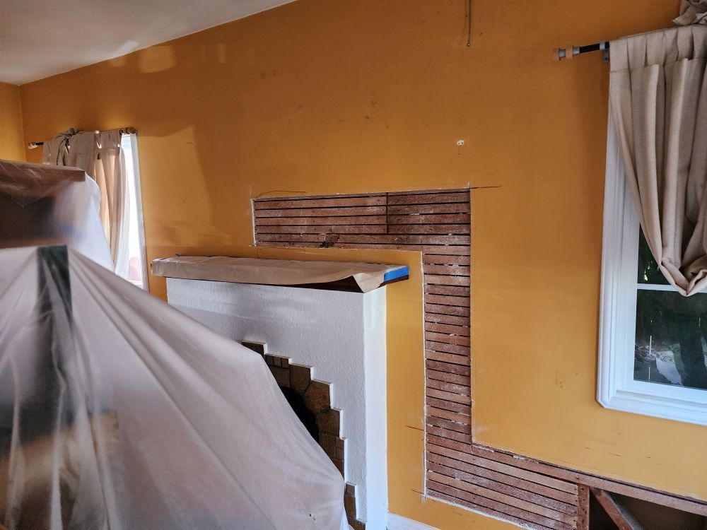 Room with an exposed wooden wall section, part of a fireplace. Yellow walls and white fireplace.