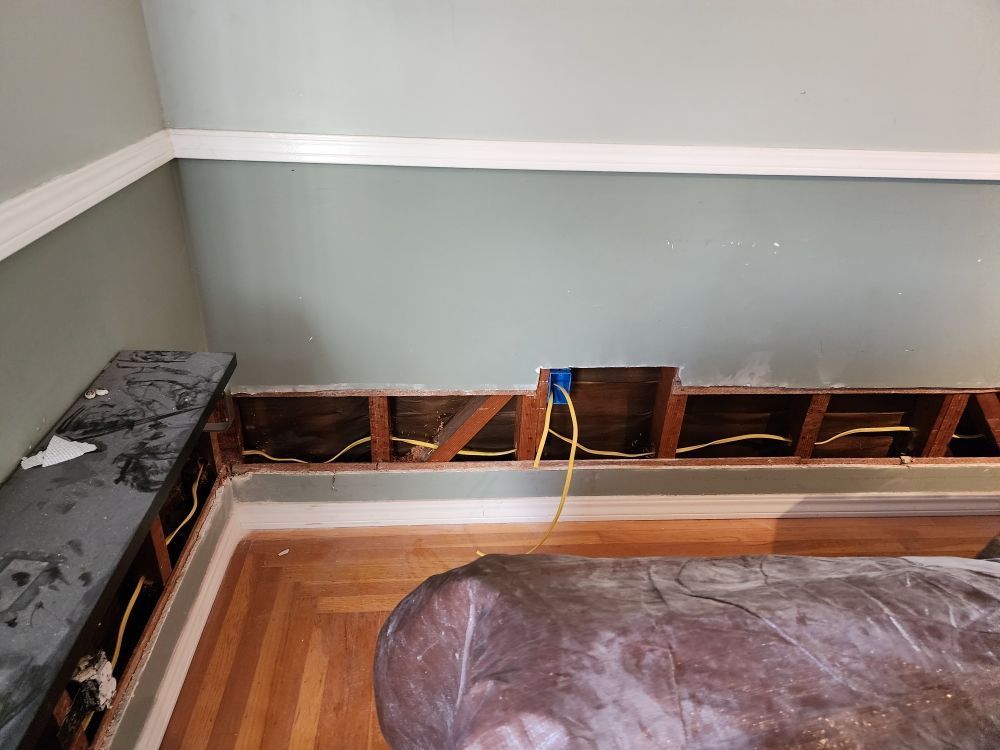 Room under renovation with exposed wall studs, electrical wires, and a partial bench.