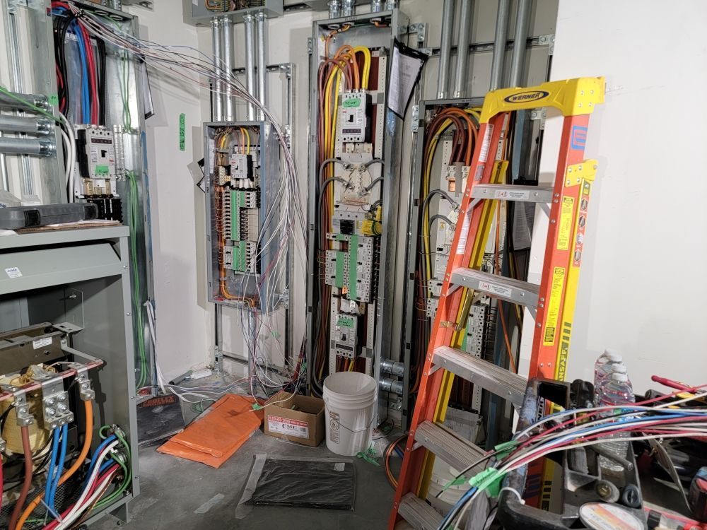 Electrical wiring in a construction site; ladder, panels, conduit, and wires in various colors.