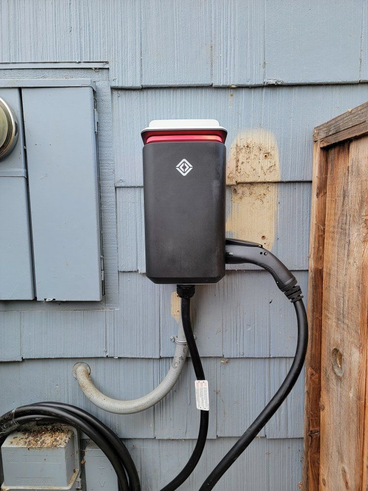 Black Rivian EV charger mounted on a blue clapboard wall next to a wooden fence.