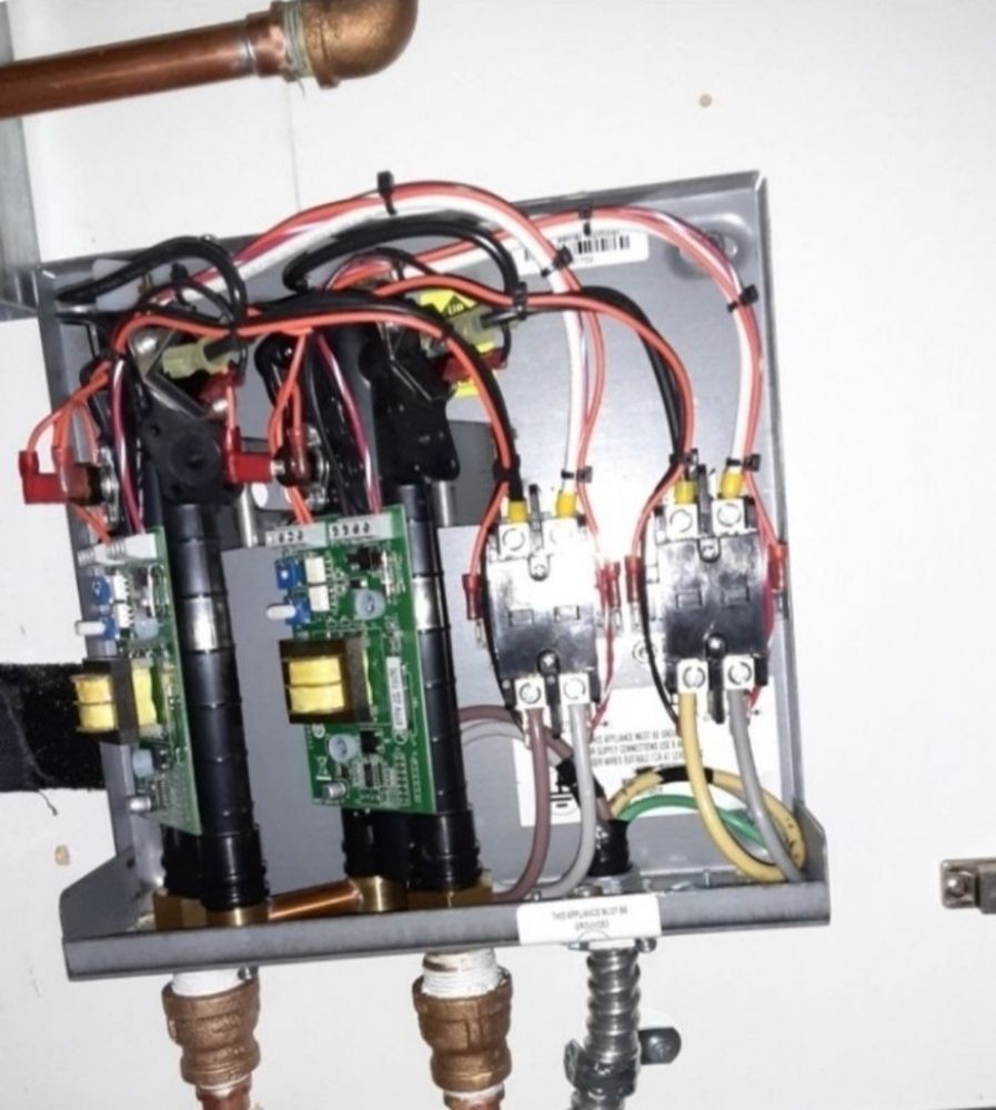 Open electrical panel with wires, circuit boards, and plumbing connections.