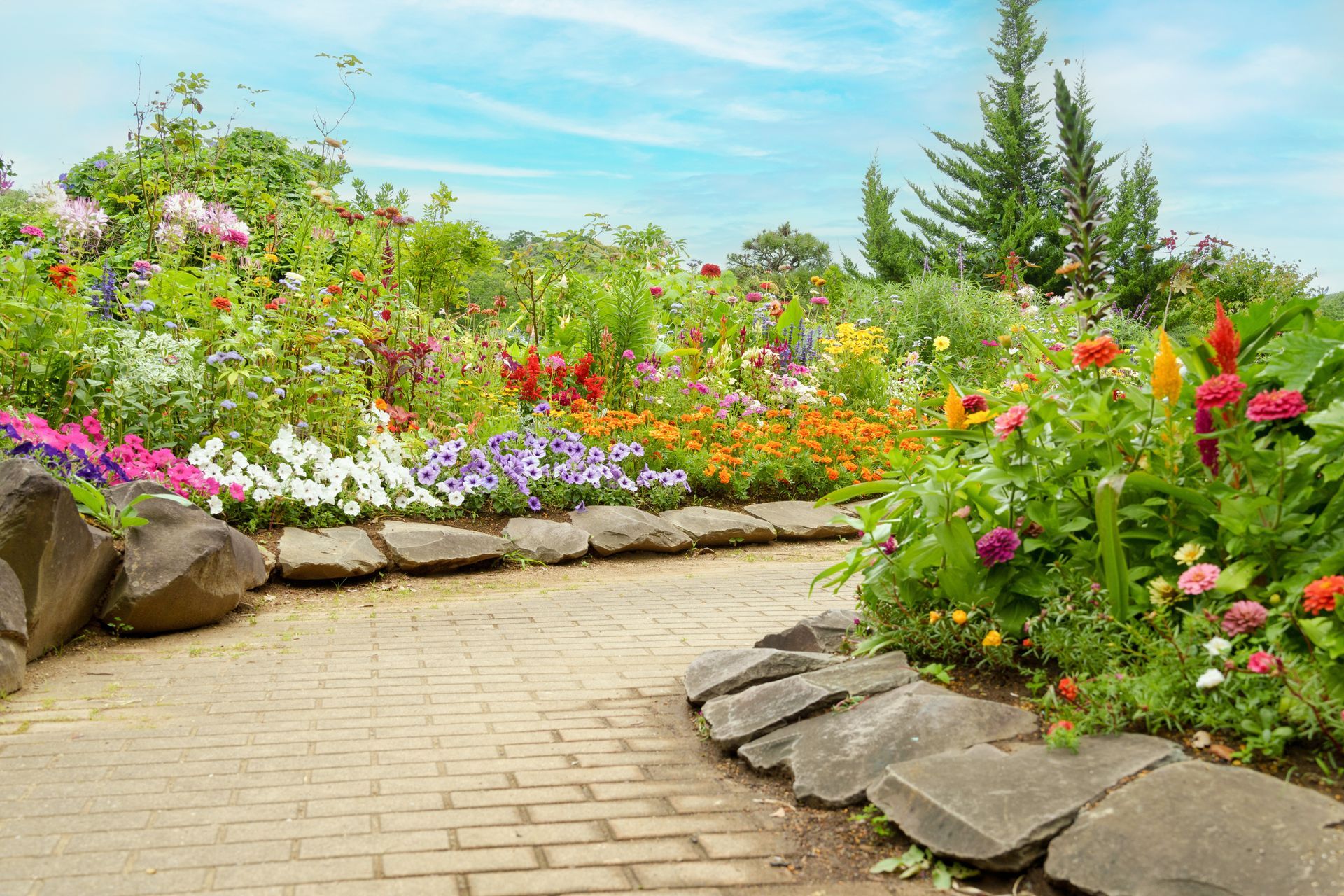A brick walkway leading to a garden filled with lots of flowers.