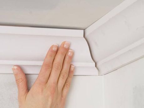 A person is touching a white molding on a wall.