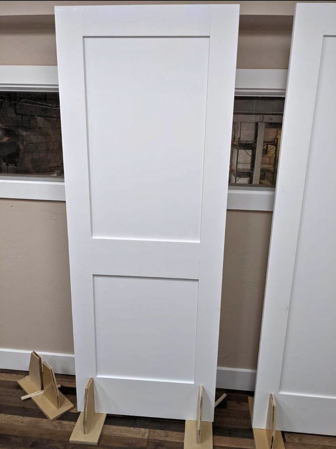 A white door is sitting on top of a wooden floor next to a window.