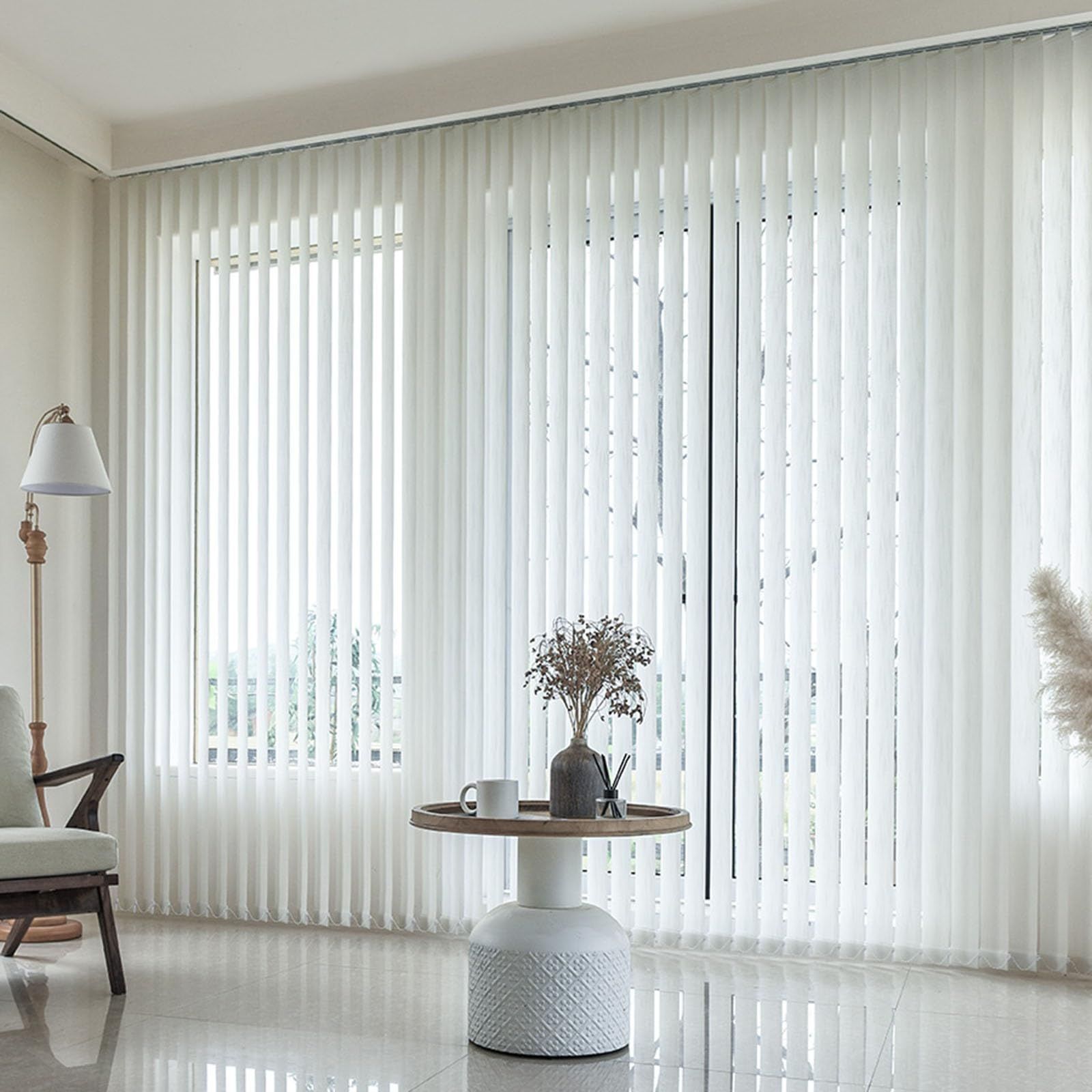 A living room with white vertical blinds and a table with a vase of flowers on it.
