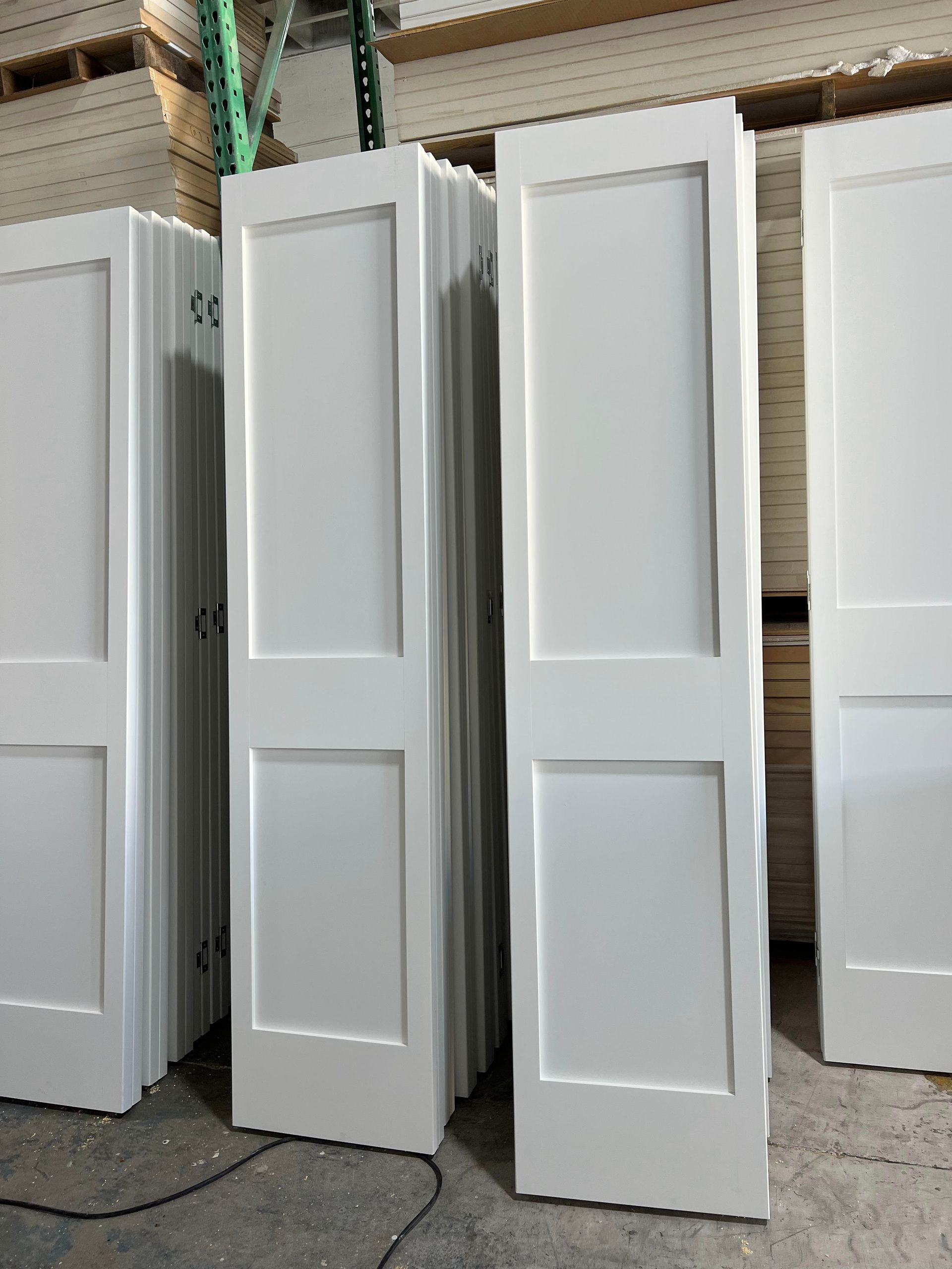 A row of white doors are stacked on top of each other in a warehouse.
