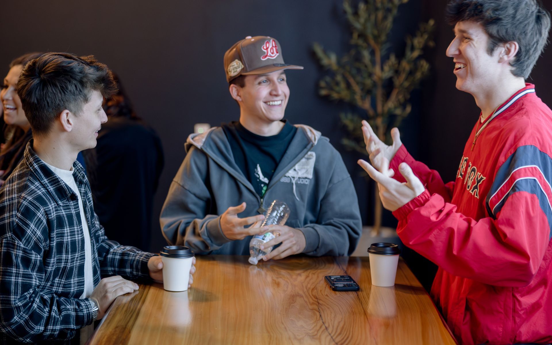 Three young men laugh while conversing at a wooden table in our coffee shop.