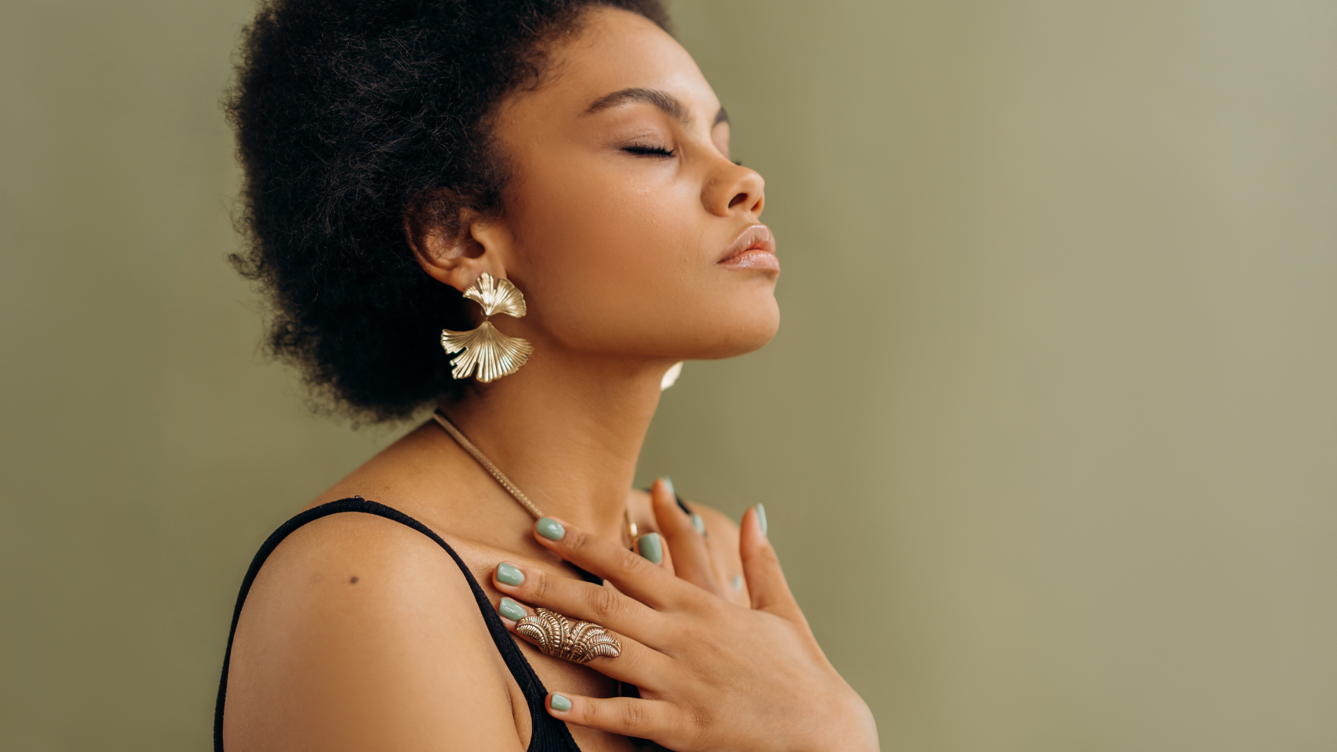 A woman wearing earrings and a necklace is holding her hands to her chest.