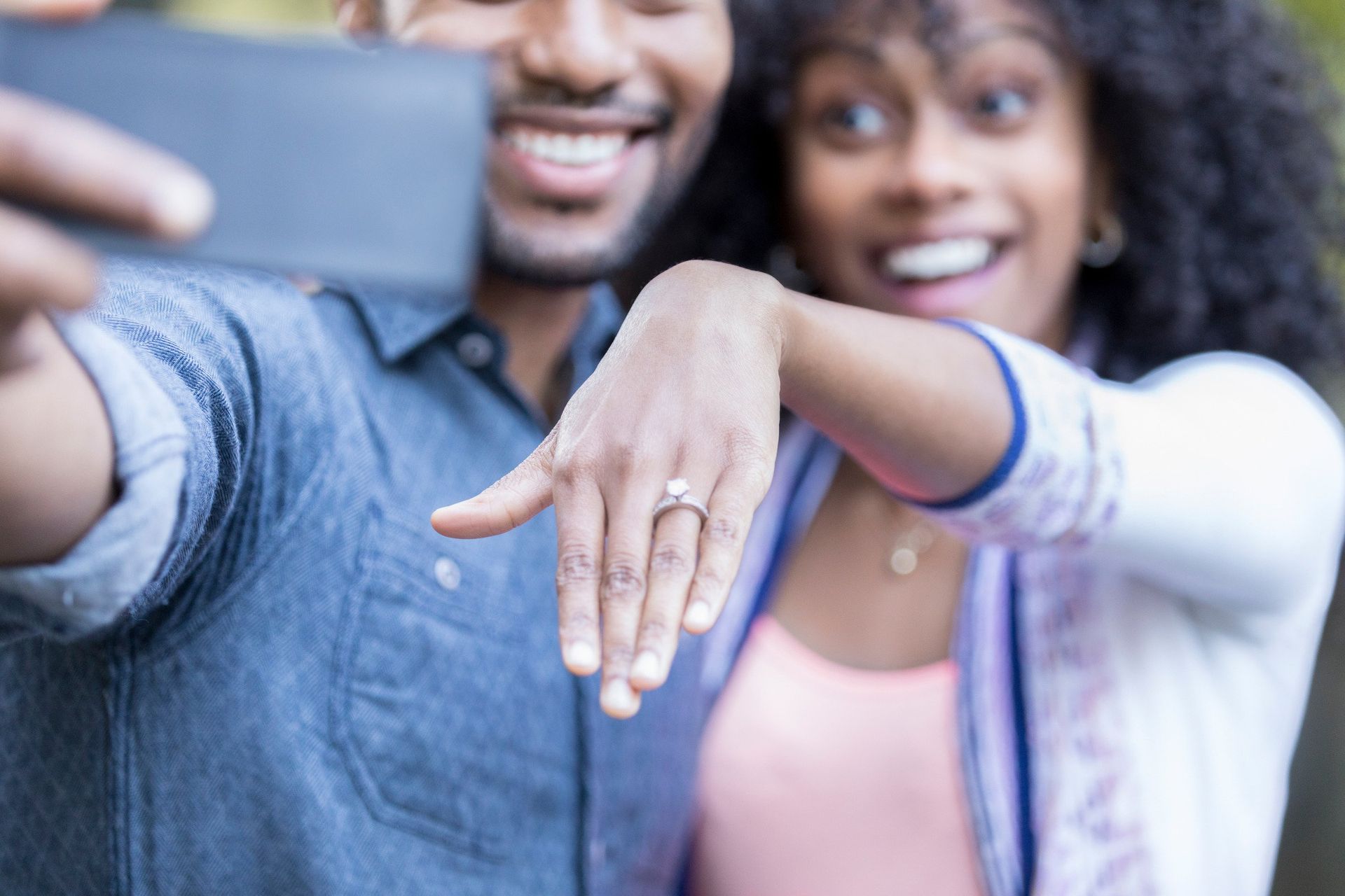 A man and woman are taking a selfie with a cell phone . the woman is wearing an engagement ring.