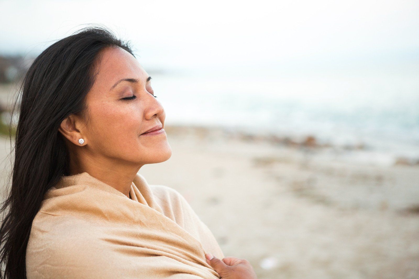 A woman is standing on a beach with her eyes closed.