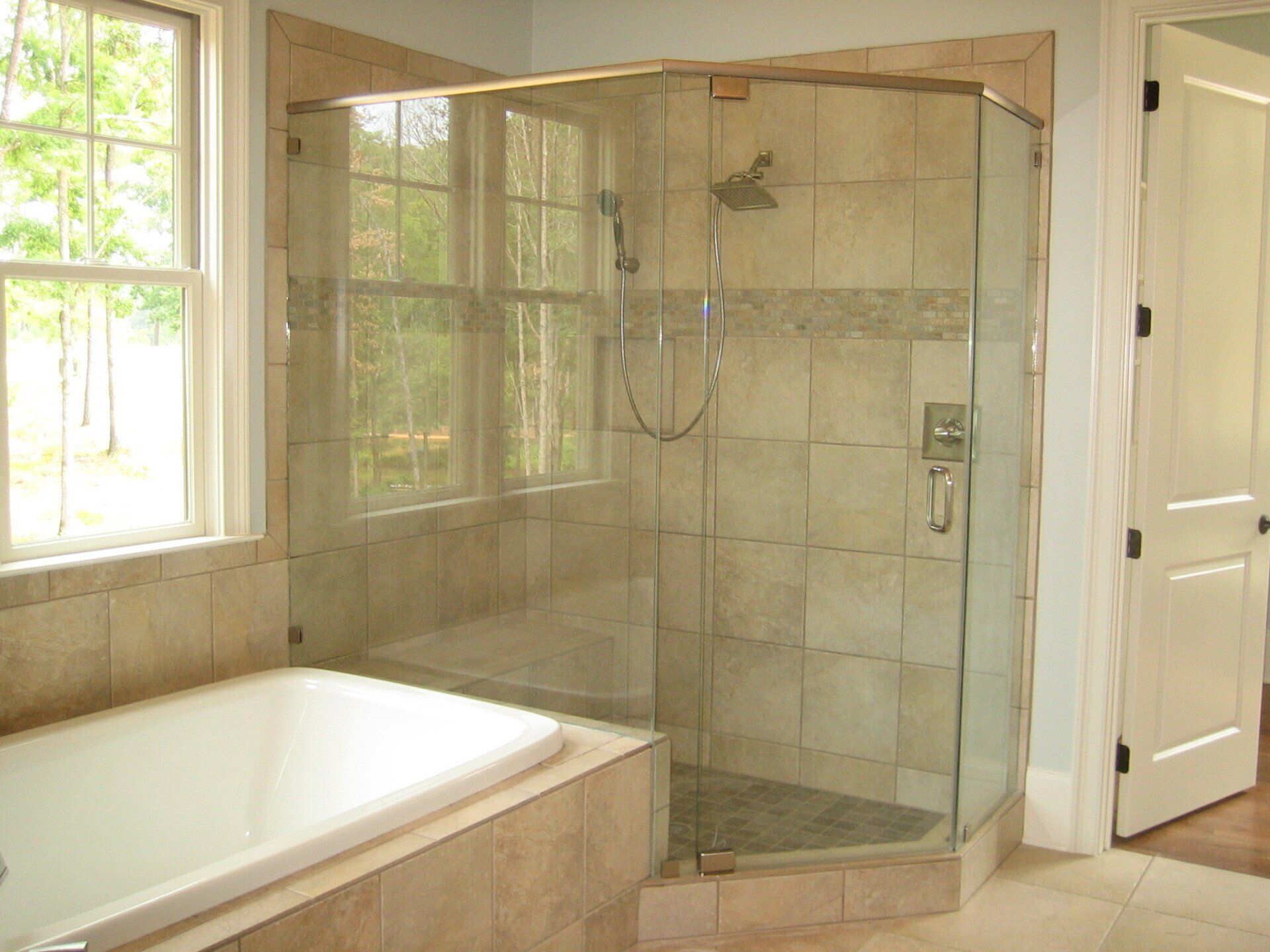 Bathroom with a glass shower, beige tile, and a white bathtub next to a window.