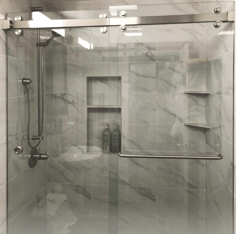 Glass shower with marble-look tile, sliding door, shelves, and showerhead.