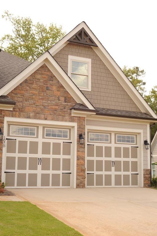 Two-car garage with light-colored doors featuring windows, set in a stone and shingle home exterior under a peaked roof.