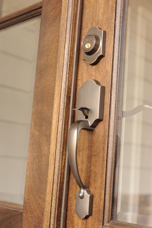 A close-up view of a matte nickel door handle and deadbolt lock on a stained wooden door with glass panels.