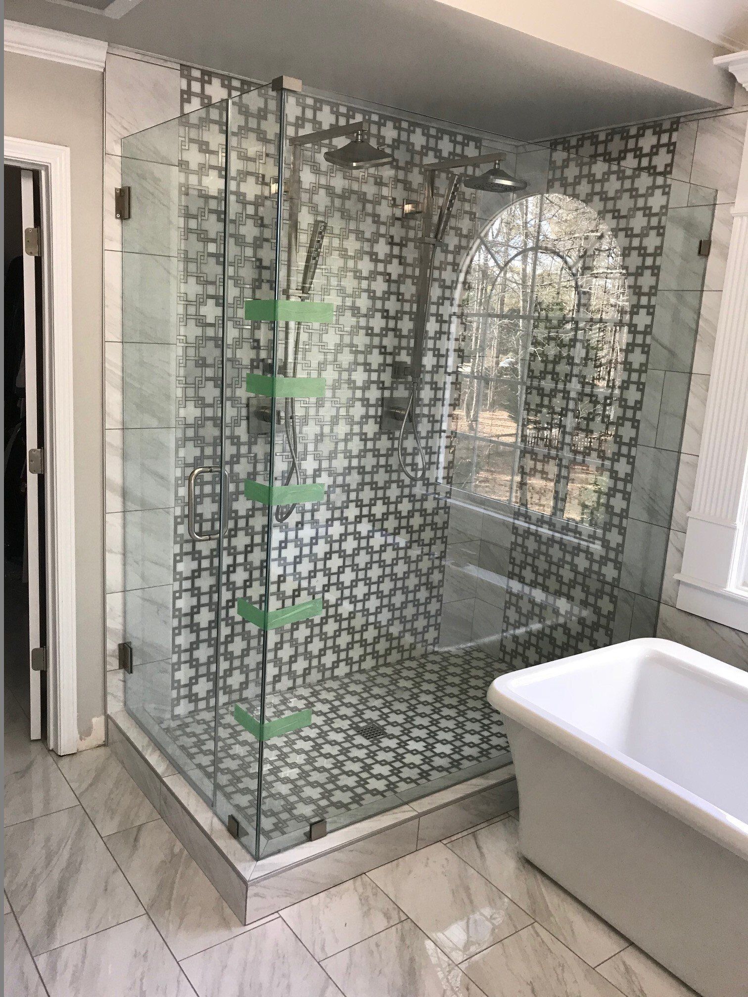 Modern bathroom with glass shower enclosure, patterned tile, and white tub.