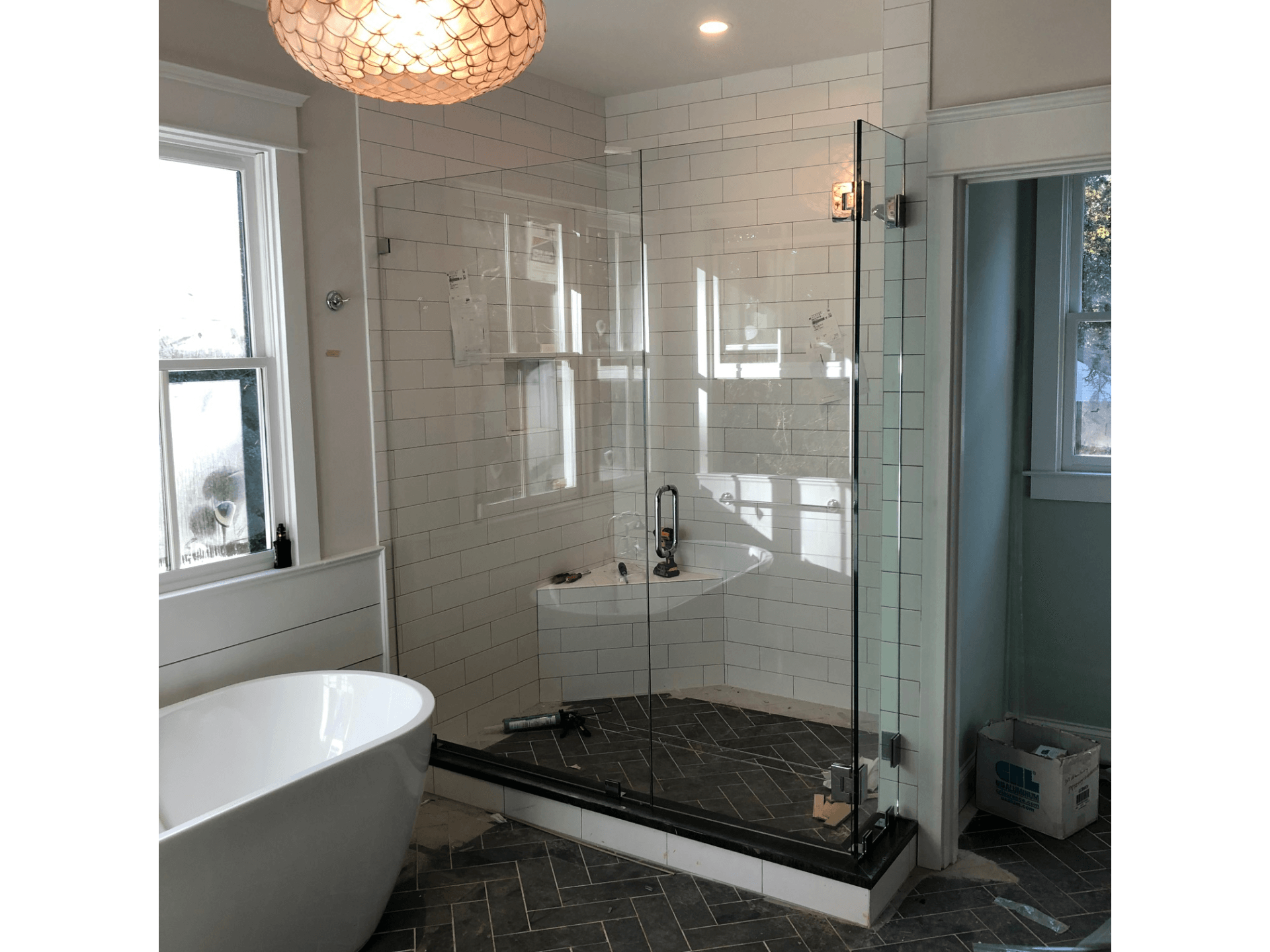 Bathroom with a glass shower, white tile, black flooring, and a freestanding tub.