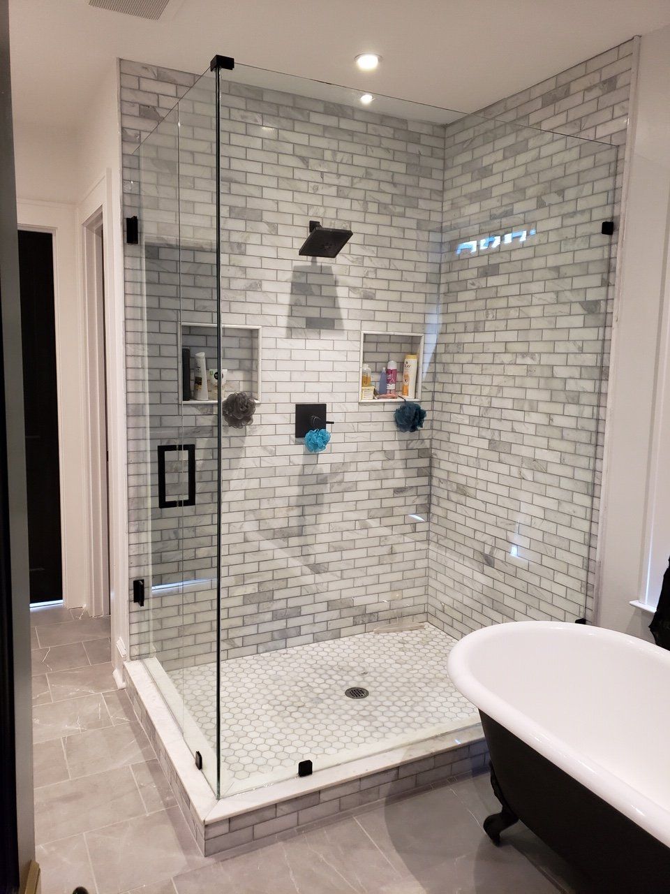 Modern bathroom with glass shower enclosure, white brick tile, black fixtures, and a freestanding tub.