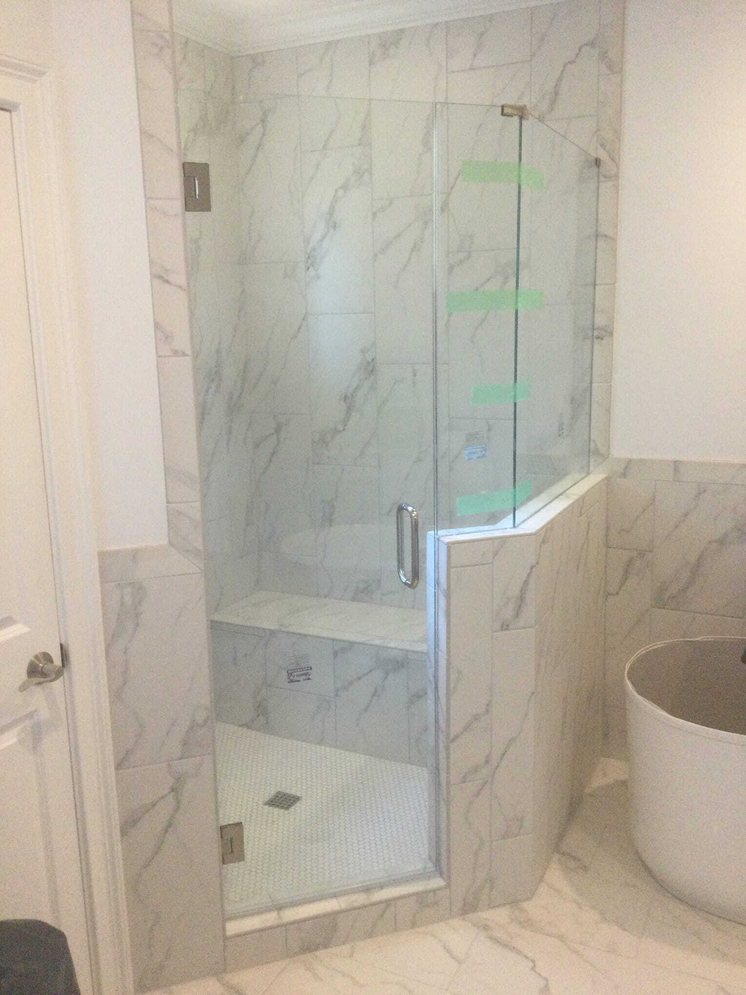 A frameless glass shower enclosure with white marble tiles and a built-in seat.