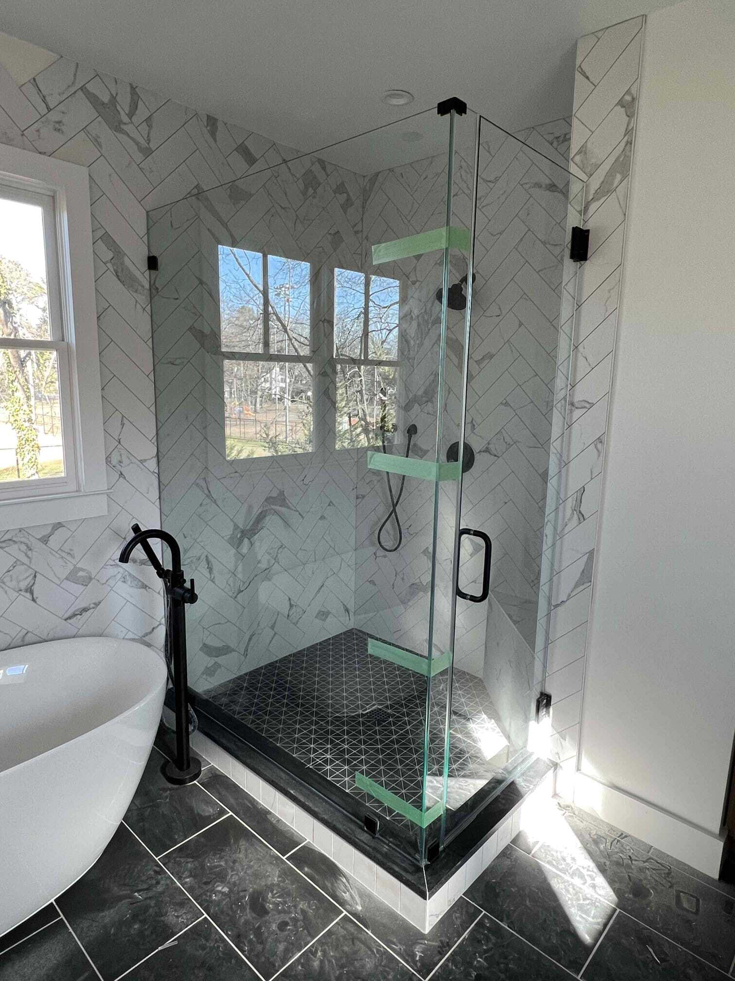 Modern bathroom with glass shower, black fixtures, herringbone tile walls, and a window.