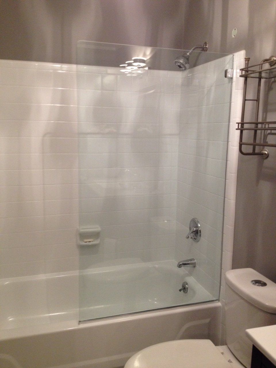 Bathroom with white tile walls, a bathtub, glass shower door, and a toilet.
