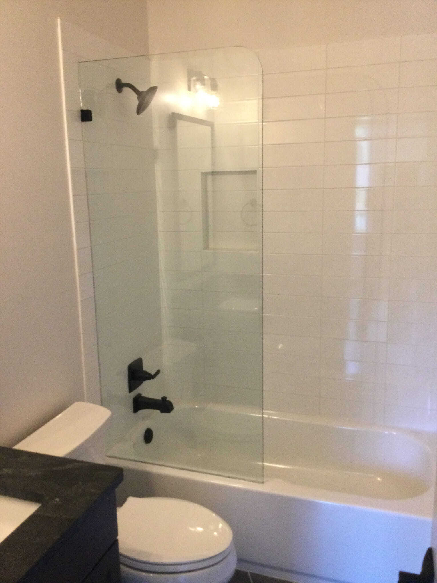 Bathroom with glass shower panel, white tiles, dark fixtures, and toilet.