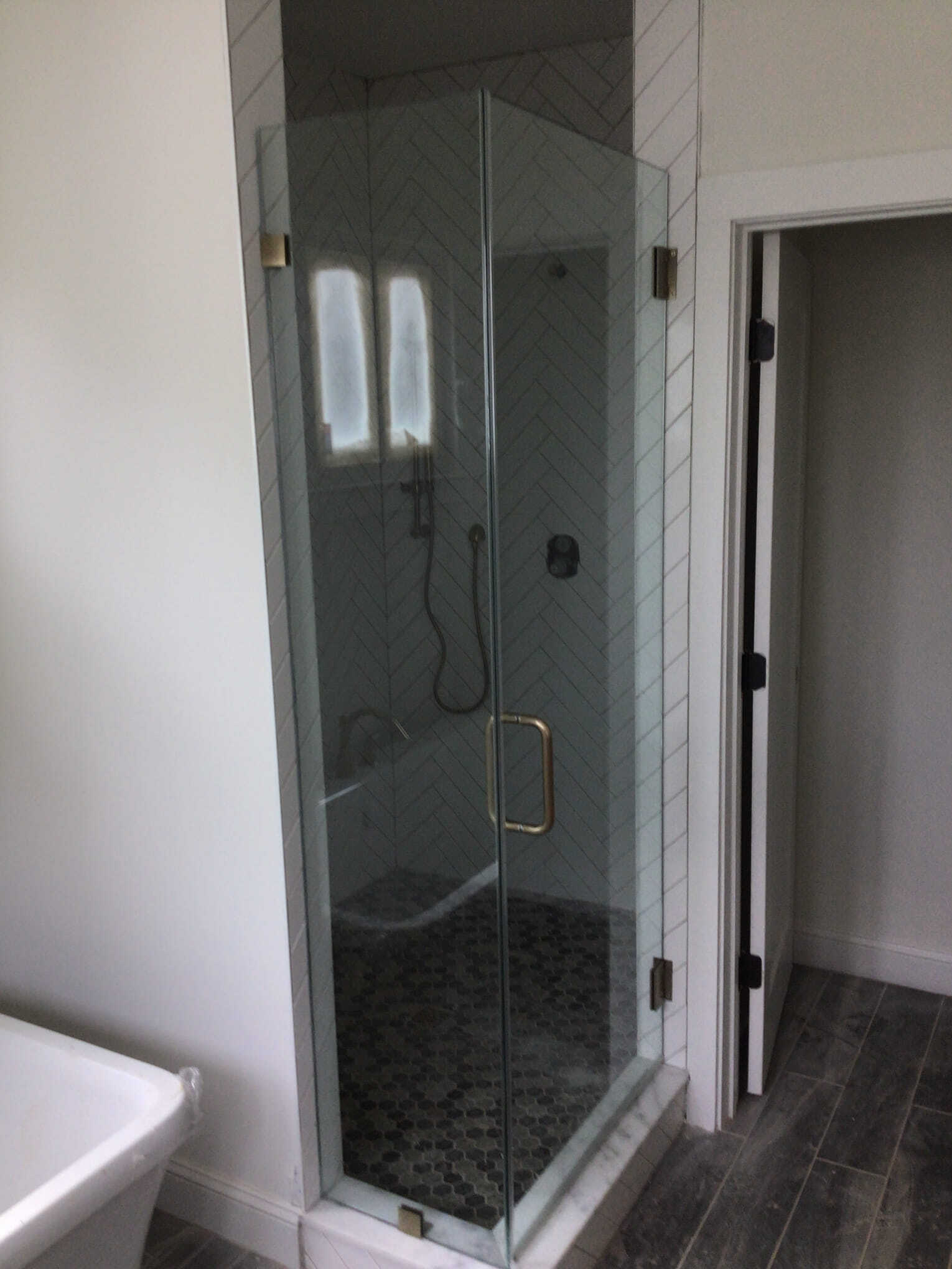 Glass shower enclosure with gold hardware, tiled walls, and small window.